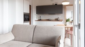 A modern living room with a beige sofa, a kitchen area with dark cabinets and a wooden countertop, and a dining area with pink chairs.