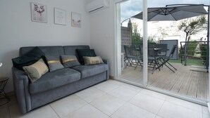 Een moderne woonkamer met een grijze bank, een glazen deur die leidt naar een terras, en een plafondventilator.
