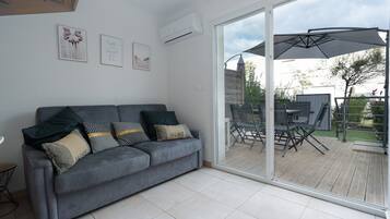 A modern living room with a grey sofa, a glass door leading to a patio, and a ceiling fan.