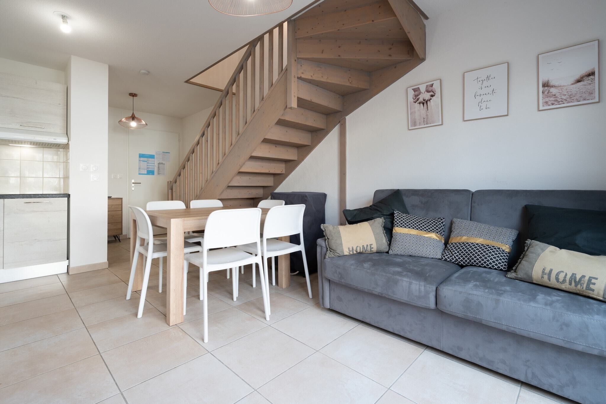 A modern living room with a grey sofa, white chairs, and a wooden staircase.