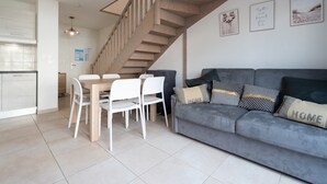 Een moderne woonkamer met een grijze bank, witte stoelen en een houten trap.