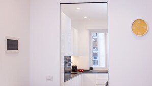 A modern kitchen with white cabinets, a black countertop, and a yellow clock on the wall.