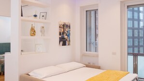 A modern bedroom with a bed, a window, and a built-in shelf with decorative items.