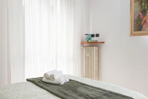 A hotel room with a bed, a towel, a radiator, and a shelf with toiletries. - Spacious Exclusive Apartment (Pioltello)