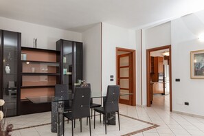 A modern dining area with a glass table and black chairs, surrounded by dark wooden cabinets with glass doors. - Spacious Exclusive Apartment (Pioltello)