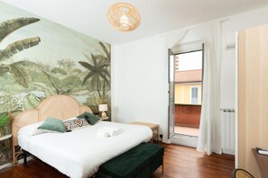 A bedroom with a bed, a nightstand, a lamp, a green bench, a mural, and a balcony door. - Flower Exclusive Apartment - M3 - Isola District (Milano)