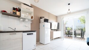 A modern kitchen with white appliances, a dishwasher, and a dining area with a table and chairs. - Charming Villa in Valras-Plage (Valras-Plage)