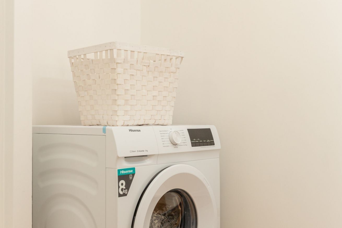 Eine Hisense Waschmaschine mit Frontlader und weißem Wäschekorb obenauf.