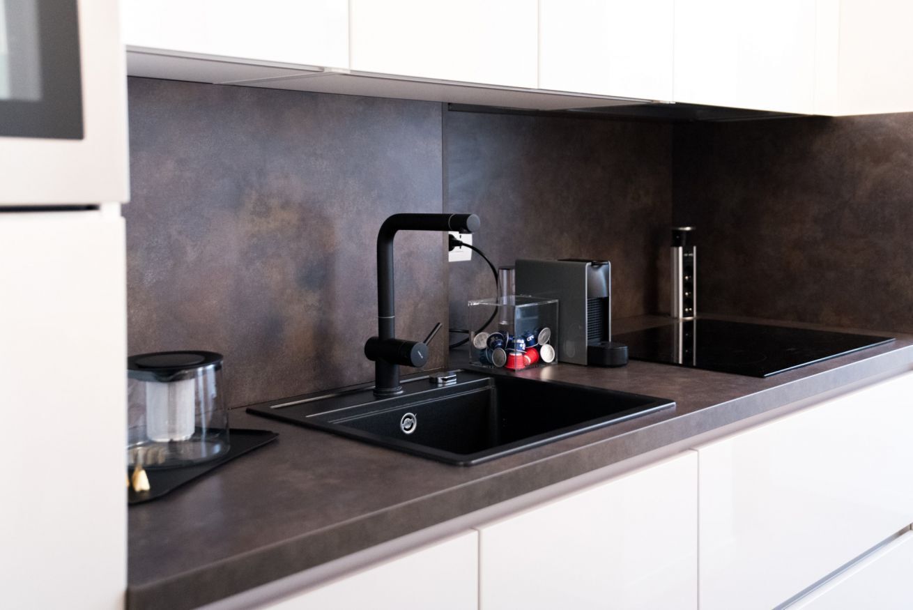 Une cuisine moderne avec un robinet noir, une machine à café et une bouilloire posés sur le plan de travail.