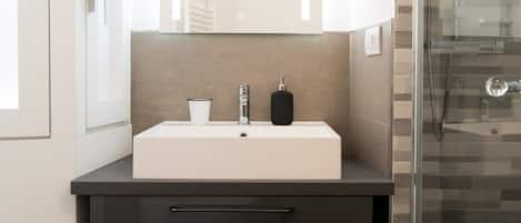 A modern bathroom with a white sink, dark countertop, and a glass shower enclosure.