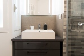 A modern bathroom with a white sink, dark countertop, and a glass shower enclosure. - Spiga - Exclusive Apartment (Milano)