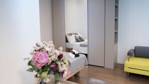 Une chambre d’hôtel moderne avec un lit, un canapé jaune, une table en bois et un vase de fleurs.