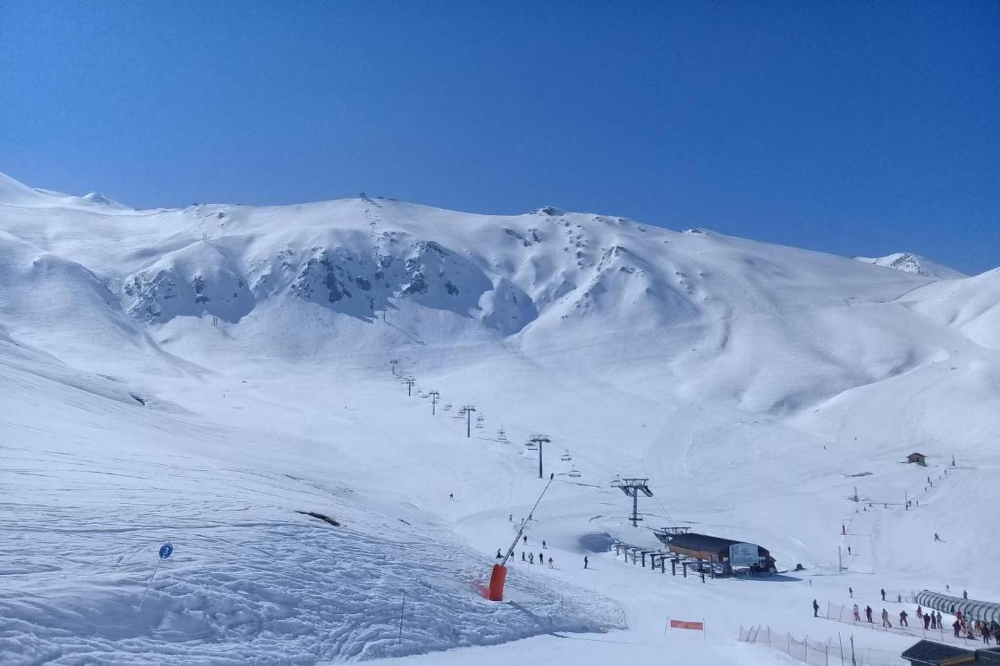 A snow-covered mountain slope with ski lifts and a small building, likely a lodge or ski rental facility.