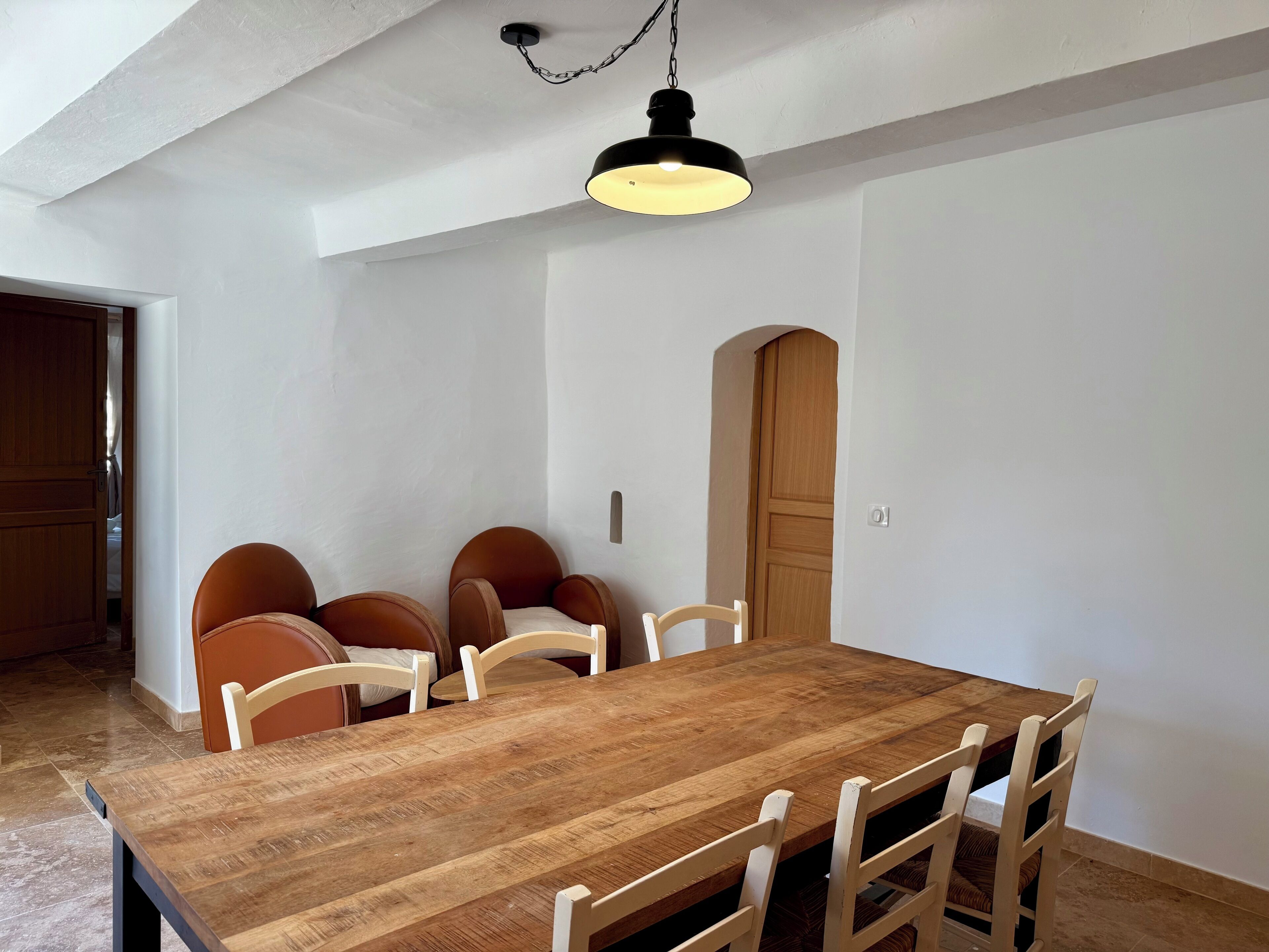 Un comedor con una mesa de madera y seis sillas, una lámpara colgante y una puerta de madera.