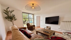 Een woonkamer met een leren bank, een bijzettafeltje met schaakspel, een televisie en een groot raam.
