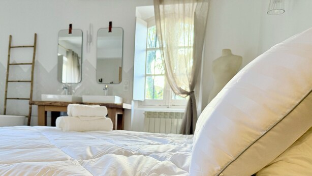 Hotelkamer met een bed, een kaptafel met spiegels, een raam met gordijnen, een radiator en een trap.