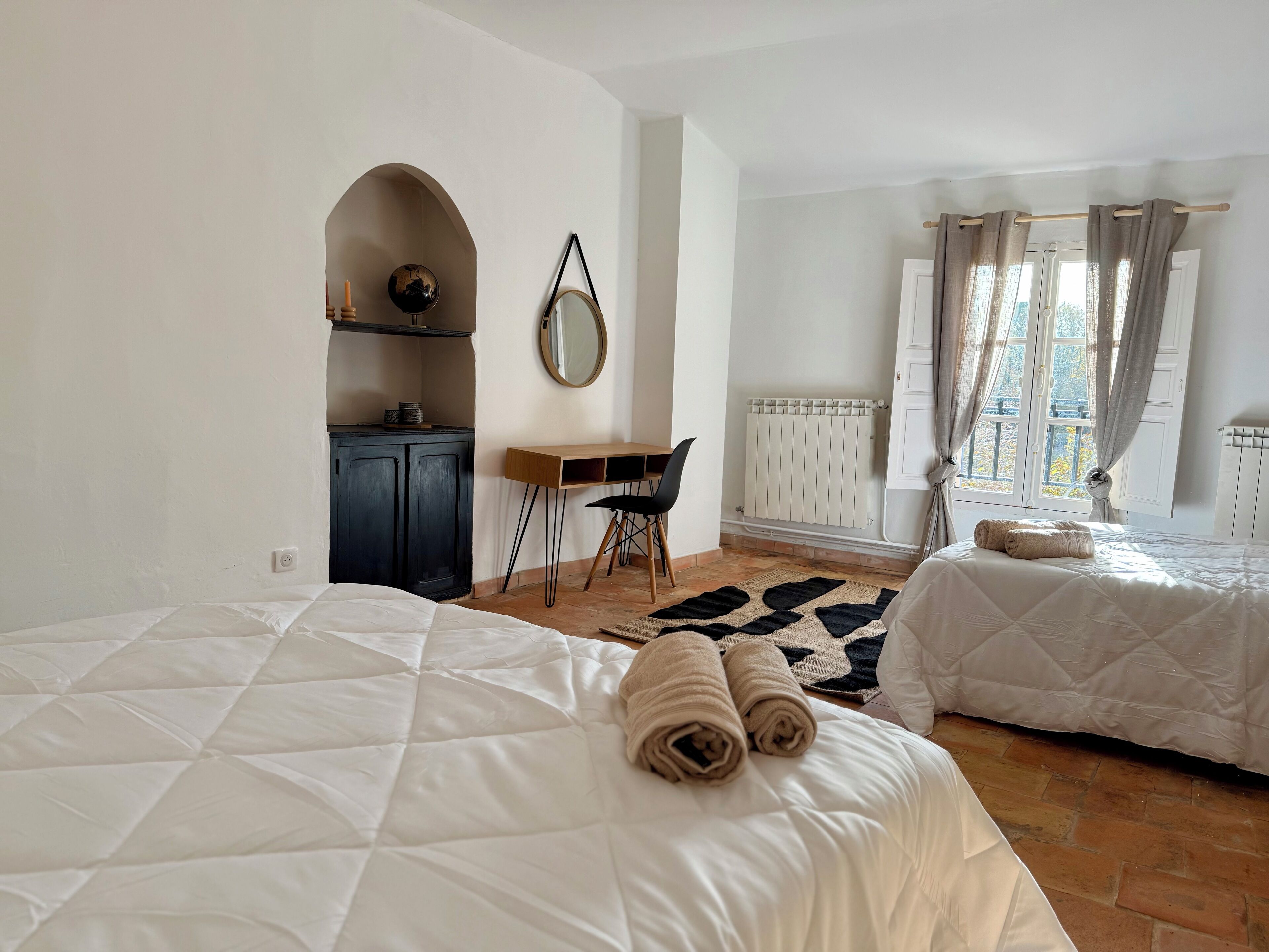 Habitación de hotel con dos camas, un escritorio, una silla, un espejo y una ventana con cortinas.