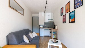 A compact living space with a sofa, a small table, a kitchenette, and a refrigerator.