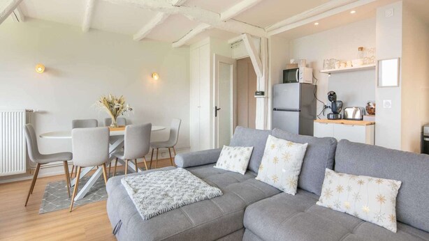 A modern living room with a grey sofa, a dining table with chairs, and a kitchen area with appliances. - Alpine Escape at Chamrousse (Chamrousse)