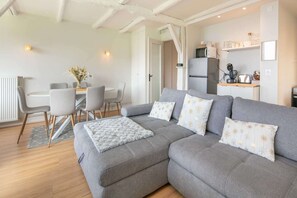 A modern living room with a grey sofa, a dining table with chairs, and a kitchen area with appliances. - Alpine Escape at Chamrousse (Chamrousse)