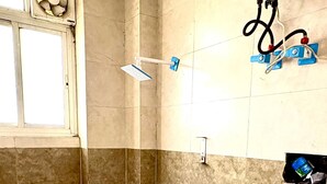 A small bathroom with a toilet, a blue bucket, a shower, and a water heater. - ICY WHITE STAY HERE (Noida)