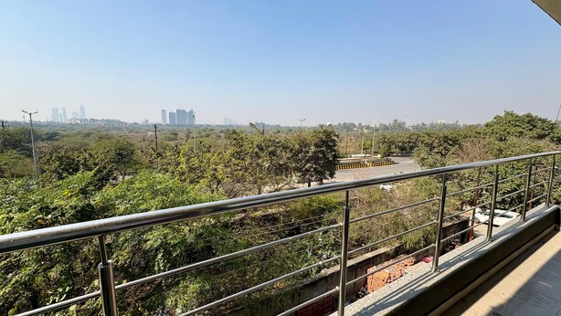 A balcony with a metal railing overlooking a green area with trees and a distant cityscape. - ICY WHITE STAY HERE (Noida)