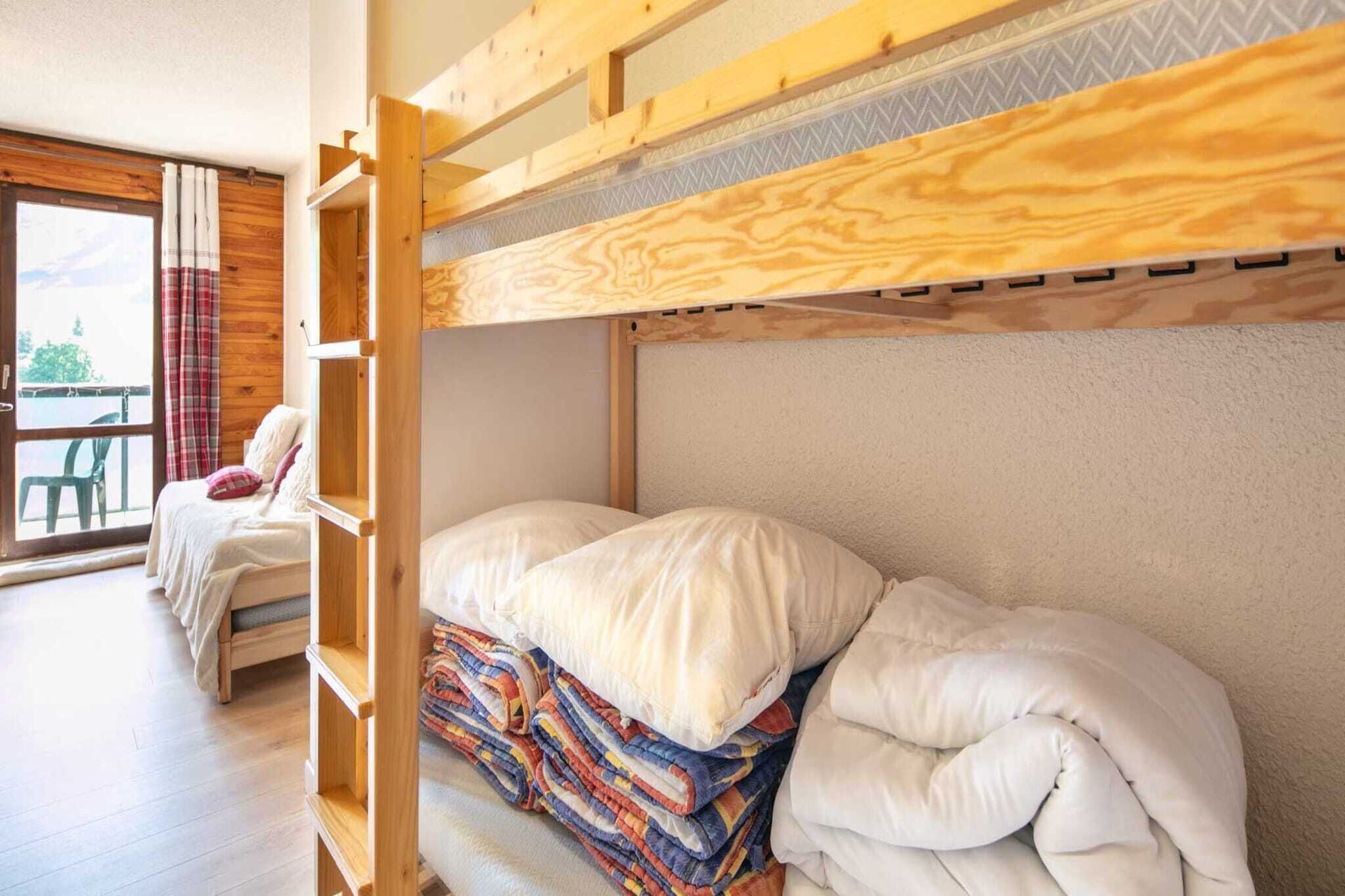 A bunk bed with a wooden headboard, a window with a view, and a chair with a plaid curtain.
