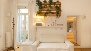 A modern living room with a white sofa, a wooden plant wall, a radiator, and a view through a glass door. - Located on the second floor of a typical Milanese condominium, this two-room apartment combines comfort and contemporary style. The flat features a fully equipped kitchen, ideal for those who love to cook and host. You will find a hob, oven, fridge, dish (Milano)