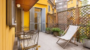 A small outdoor patio with a metal table and chairs, a cushioned lounge chair, and a wooden fence. - Located on the second floor of a typical Milanese condominium, this two-room apartment combines comfort and contemporary style. The flat features a fully equipped kitchen, ideal for those who love to cook and host. You will find a hob, oven, fridge, dish (Milano)