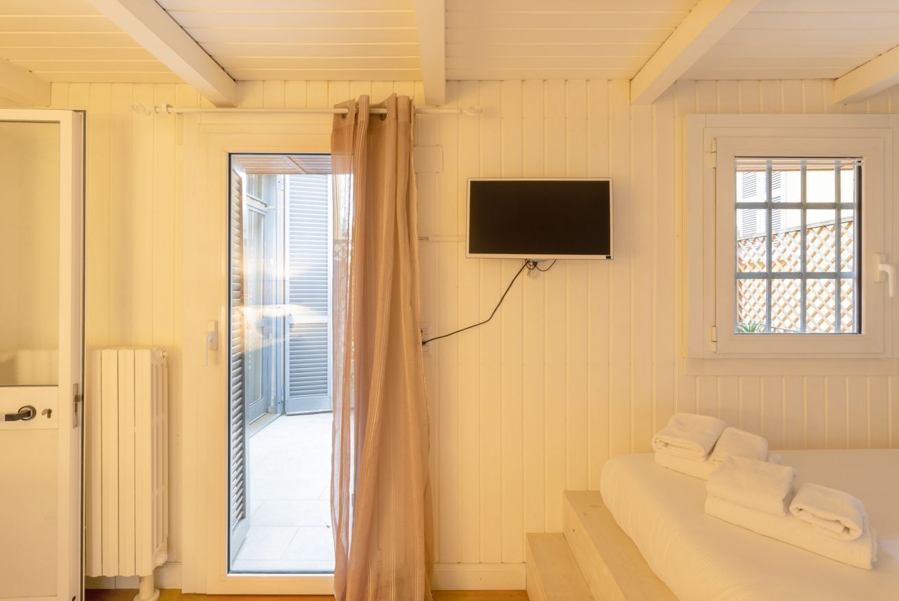 A room with a bed, a TV mounted on the wall, a window with a lattice, and a door leading to an outdoor area.