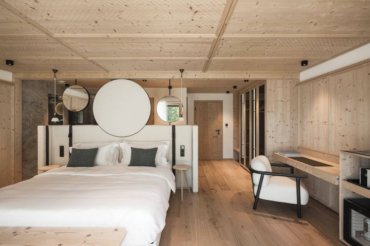 A modern bedroom with a wooden ceiling, a large bed, a bedside table, a chair, and a built-in desk with a mirror.