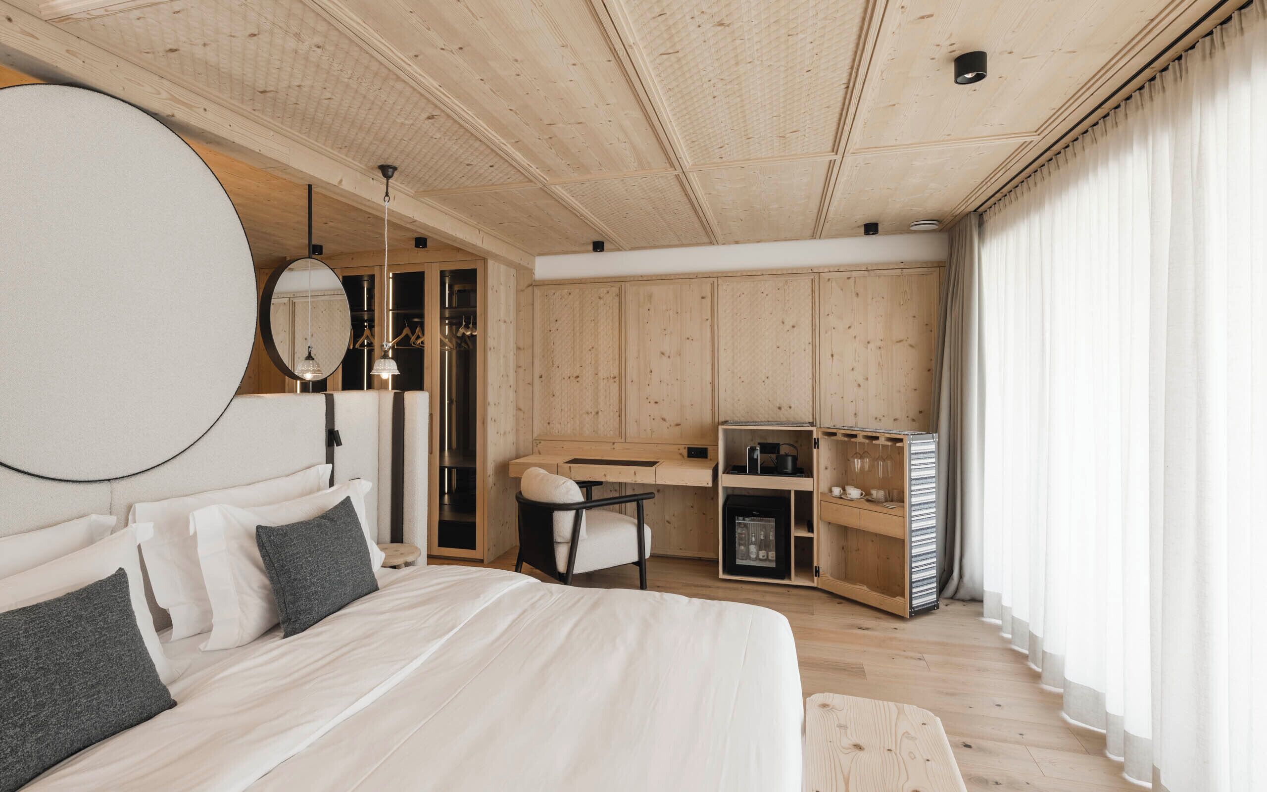 A modern bedroom with a large bed, a desk, and a wardrobe.