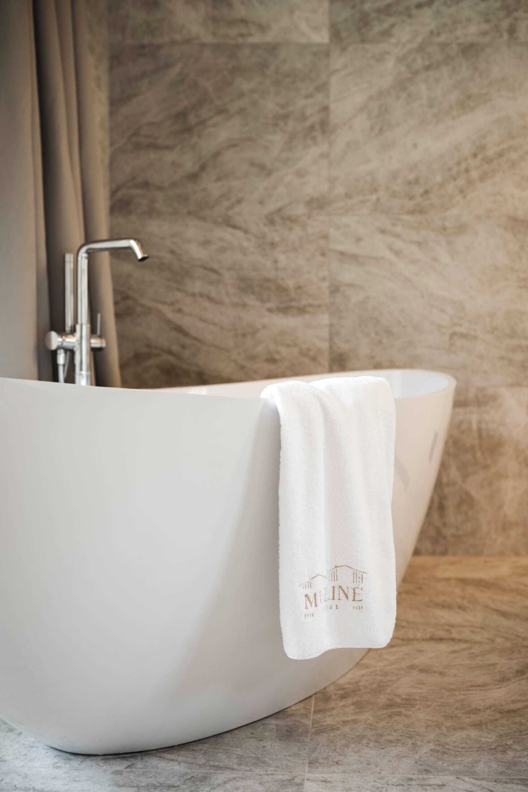 A white bathtub with a towel hanging on the side, a faucet, and a marble wall in the background.