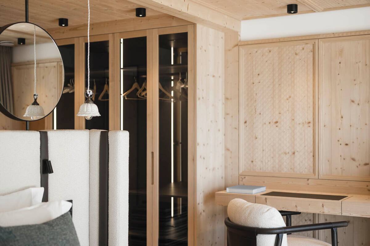 A modern bedroom with a bed, bedside table, chair, and a walk-in closet with a mirror and hanging clothes.