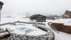 Ein verschneites Freigelände mit Pool, Holzbauten und einem Holzzaun.