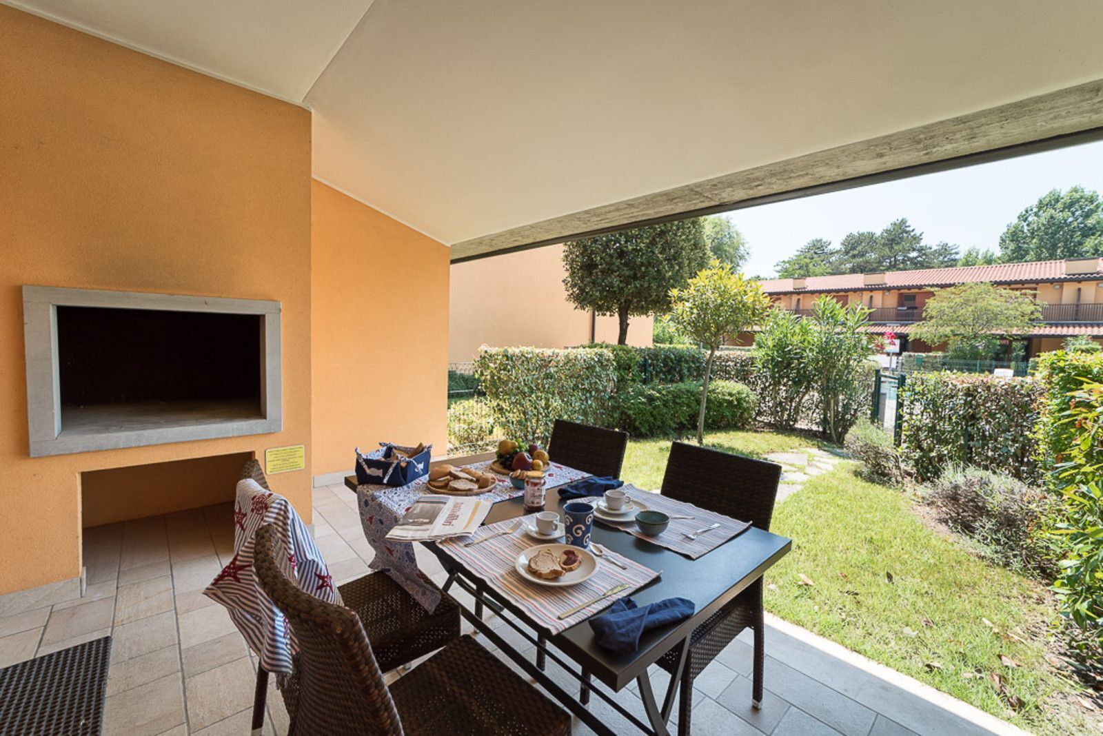 Un comedor con una mesa dispuesta para dos personas, un televisor de pantalla plana en la pared y vistas al jardín y edificios exteriores.