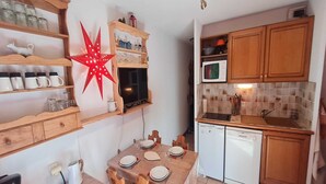 A compact kitchen with wooden cabinets, a microwave, a sink, and a dining table set for four.