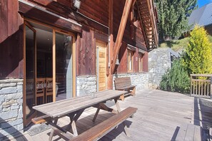 A wooden cabin with a stone exterior, large sliding glass doors, and a wooden deck with picnic tables. - Spacious Chalet Near Ski Slopes (Les Deux Alpes)