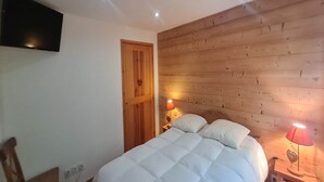 Un dormitorio con una cama, paneles de madera en las paredes, un televisor montado y dos lámparas de noche.
