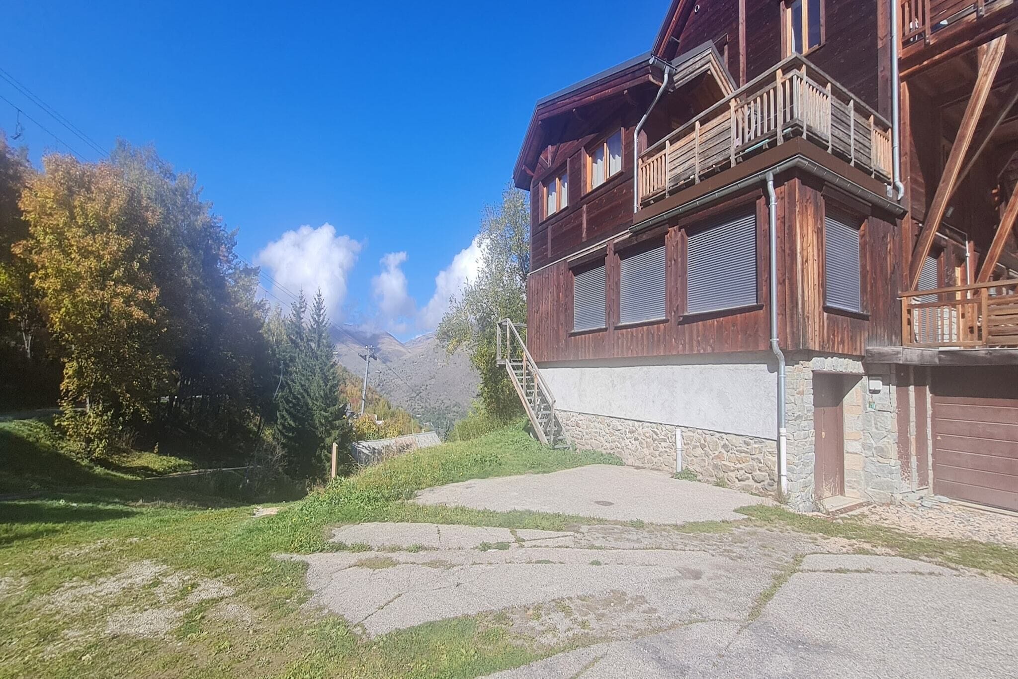 Un edificio de madera con balcón, un camino de piedra y montañas al fondo.