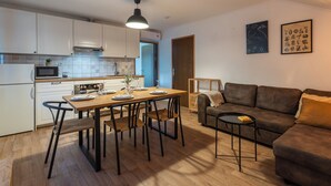 Eine moderne Küche mit weißen Schränken, einem Esstisch mit Stühlen, einem braunen Sofa und einem kleinen Beistelltisch.