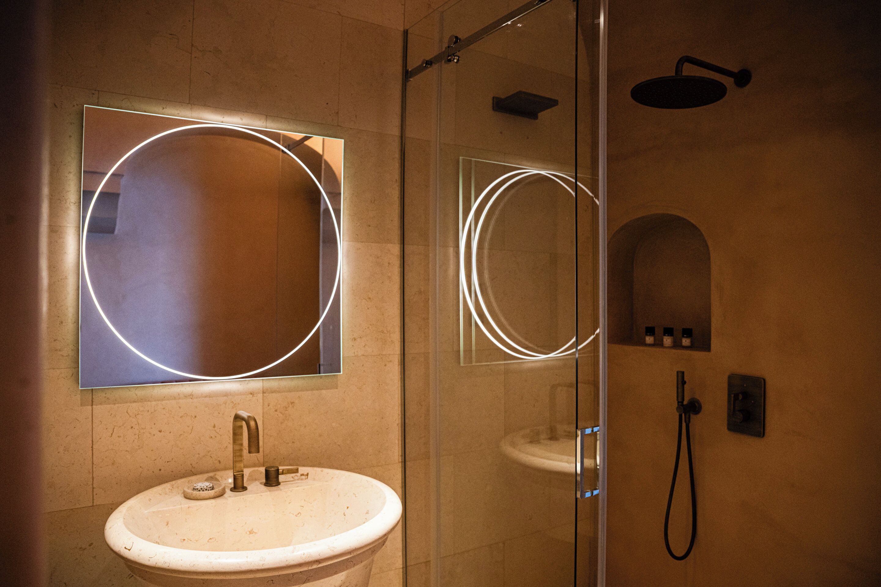 A bathroom with a round mirror, a sink, and a shower.