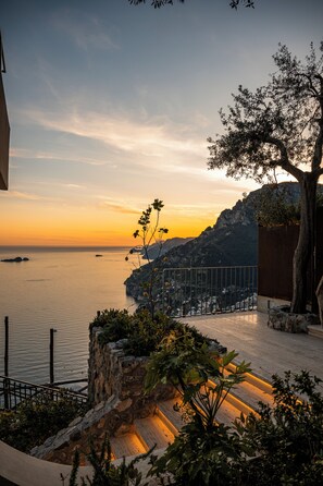A coastal view with a sunset, a stone staircase, and a railing overlooking the sea. - Antalia Boutique Hotel (Positano)