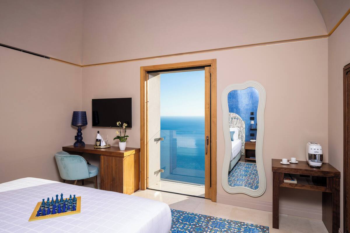Habitación de hotel con cama, escritorio, silla, televisor, cafetera y vista al mar.