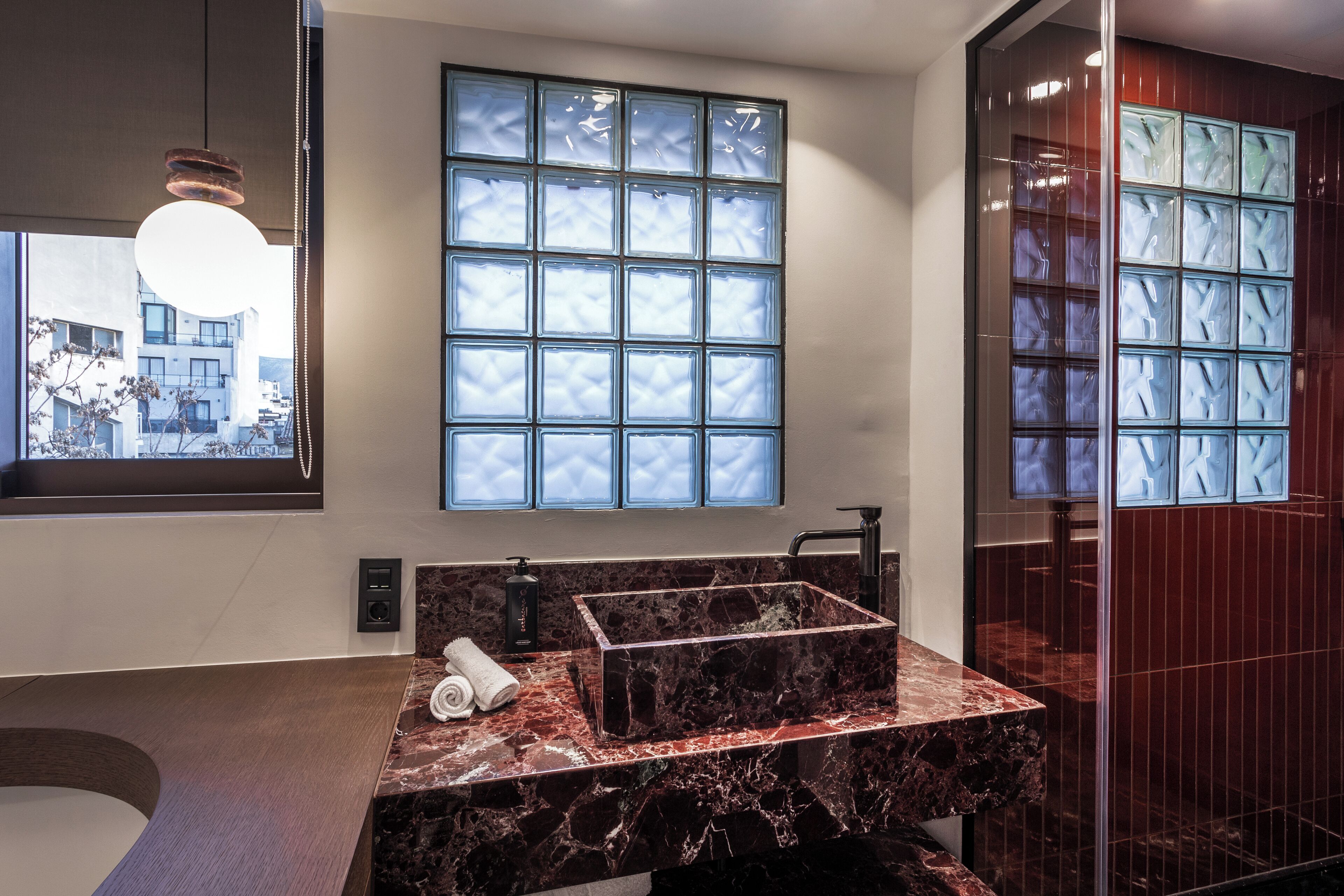 A modern bathroom with a marble sink, a large window with frosted glass panels, and a shower area with a glass door.