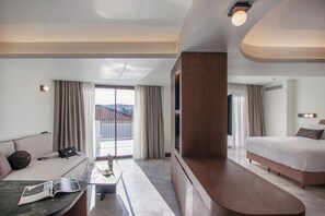 A modern hotel room with a large bed, a sofa, a dining table, and a TV. - L'Avventura Suites  (Athens)