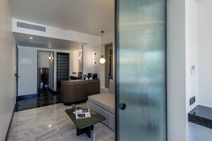 A modern hotel lobby with a reception desk, seating area, and a glass door leading to a bathroom.
