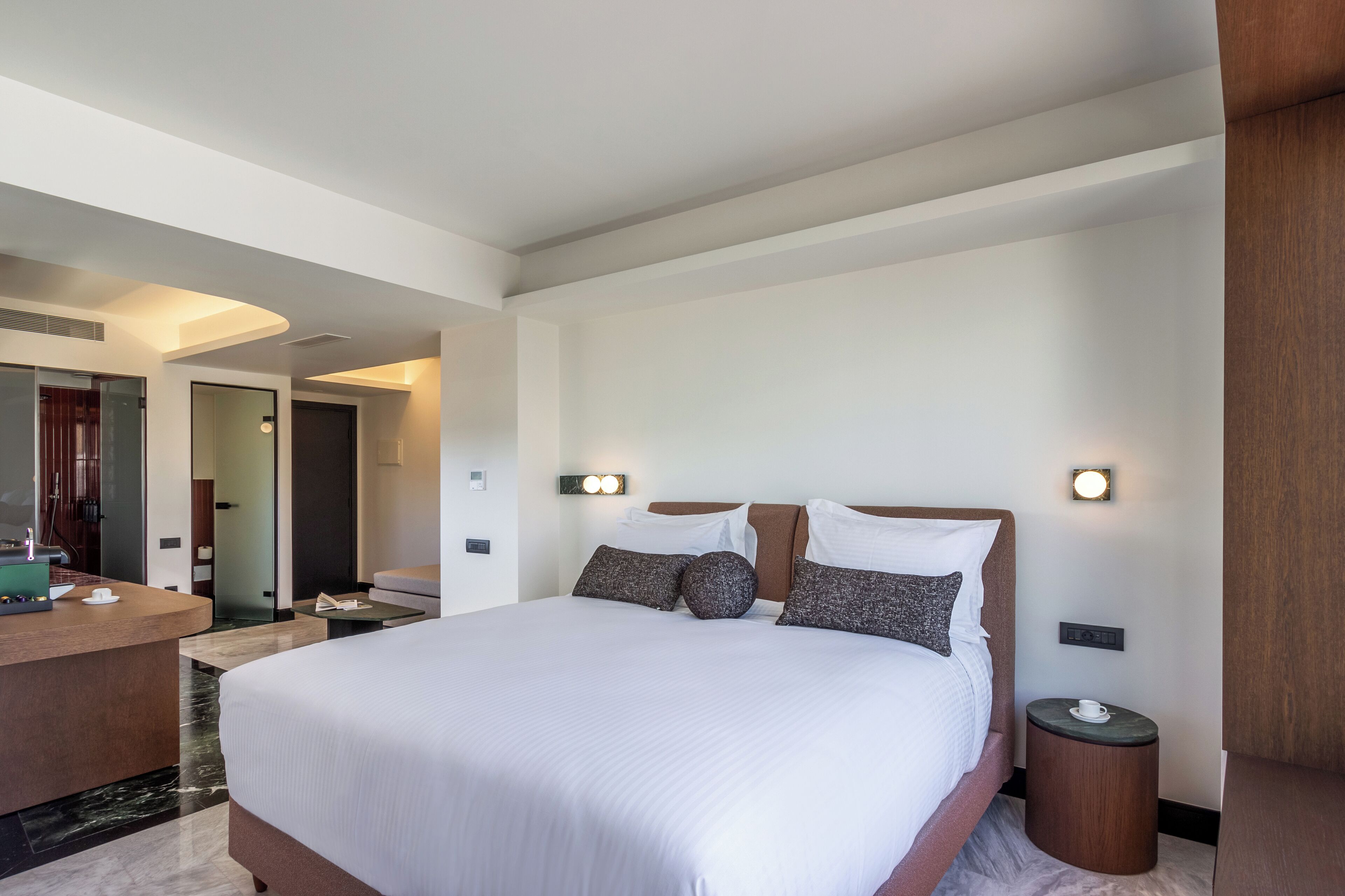 A modern hotel room with a large bed, bedside tables, a desk, and a mirror.