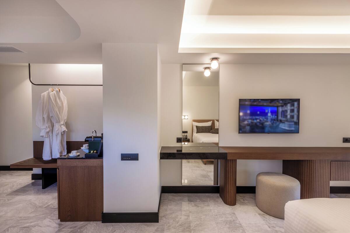 A modern hotel room with a wooden desk, a mirror, a television, and a bed.