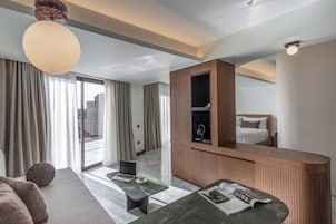 A modern hotel room with a large bed, a desk, a laptop, and a view of the city through the window.